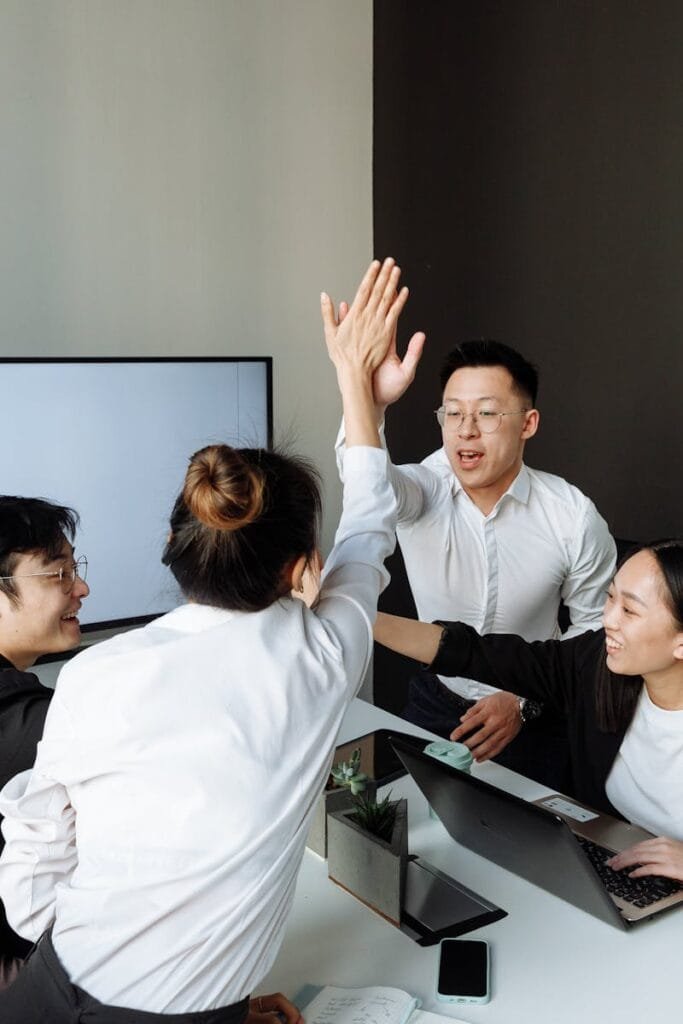 A group of Asian colleagues high-fiving in an office during a business meeting, showcasing teamwork and success.
